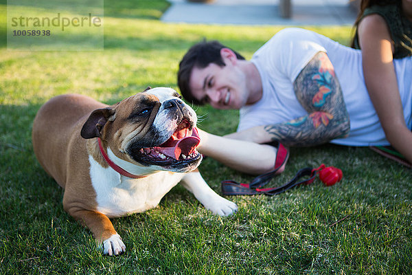 Junger Mann liegt im Park und streichelt die Bulldogge.