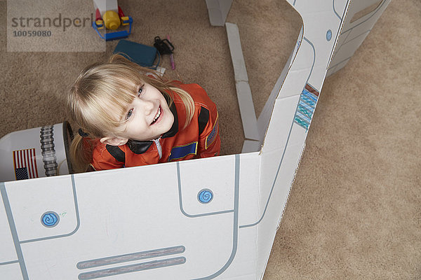 Junges Mädchen spielt im Papp-Raumschiff  trägt Astronauten-Outfit  erhöhte Ansicht