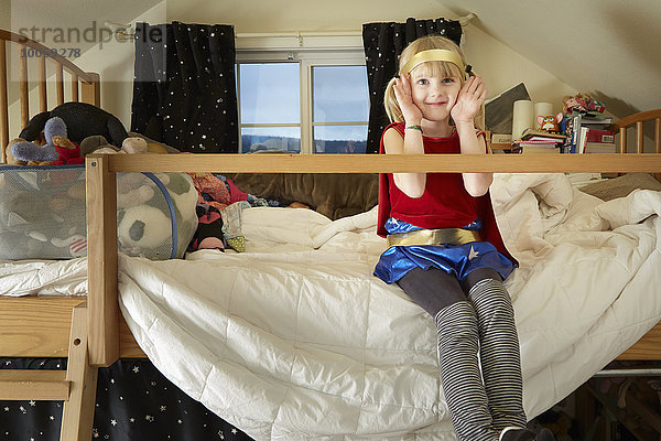 Porträt eines jungen Mädchens  das auf dem Bett sitzt und ein Kostüm trägt.
