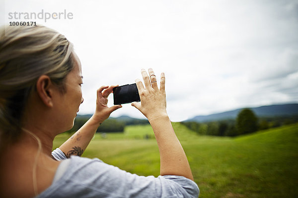 Frau beim Fotografieren auf dem Smartphone der ländlichen Feldlandschaft