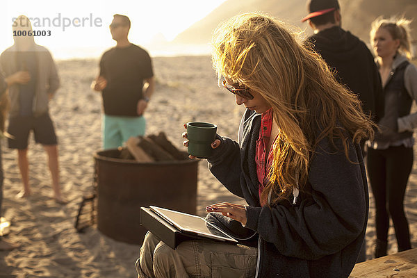 Frau mit digitalem Tablett am Strand  Freunde im Hintergrund