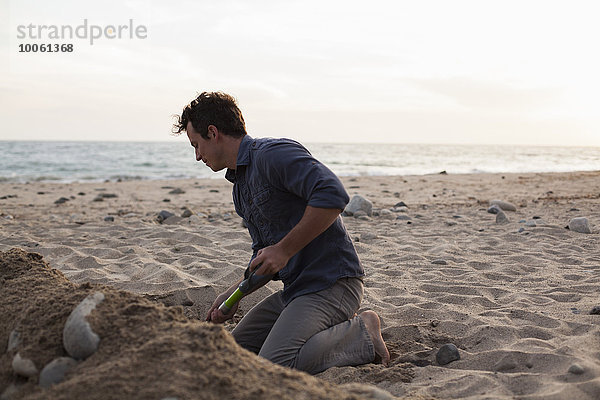 Mann  der am Strand in Sand gräbt