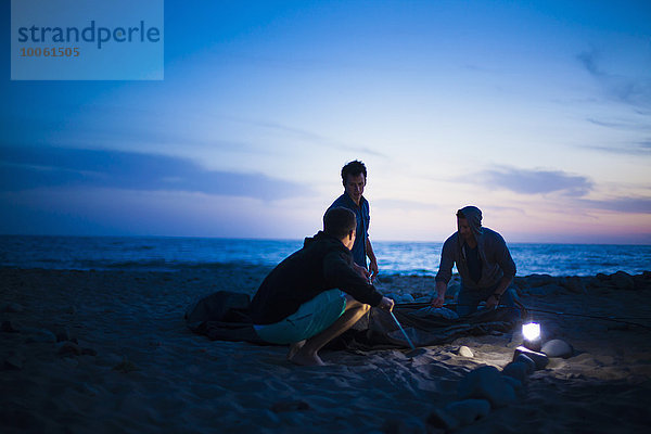 Gruppe von Freunden baut bei Sonnenuntergang ein Zelt am Strand auf.