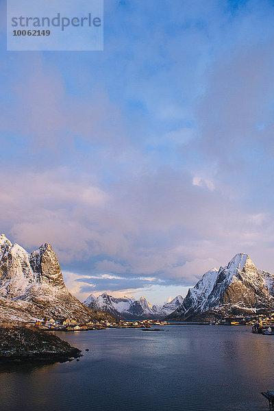 Fernsicht auf das Dorf am Wasser und die schneebedeckten Berge bei Dämmerung  Reine  Lofoten  Norwegen