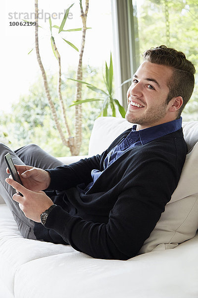 Porträt eines Mannes  der sich auf dem Sofa entspannt  mit hochgeklappten Füßen  die ein digitales Lesegerät halten.