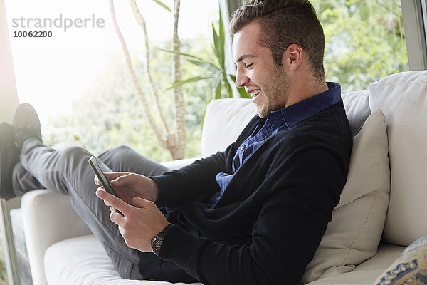 Porträt eines Mannes  der sich auf dem Sofa entspannt und mit den Füßen nach oben auf das digitale Lesegerät schaut.