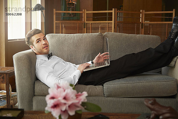 Porträt eines Mannes in schicker Kleidung auf dem Sofa liegend mit Laptop