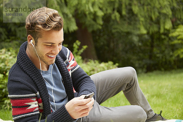 Porträt eines Mannes  der im Garten liegt und Smartphones mit Kopfhörern hört.
