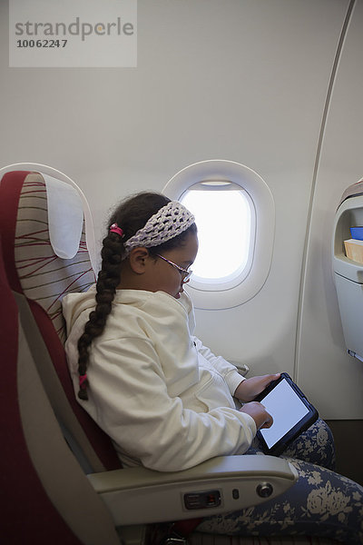 Junges Mädchen sitzend im Flugzeug mit digitalem Tablett