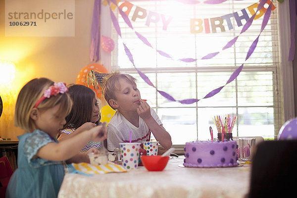Drei Kinder sitzen am Tisch und essen lila Geburtstagskuchen.