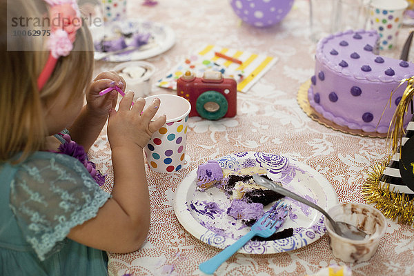 Seitenansicht des Mädchens  das am Geburtstagstisch sitzt und lila Kuchen isst.