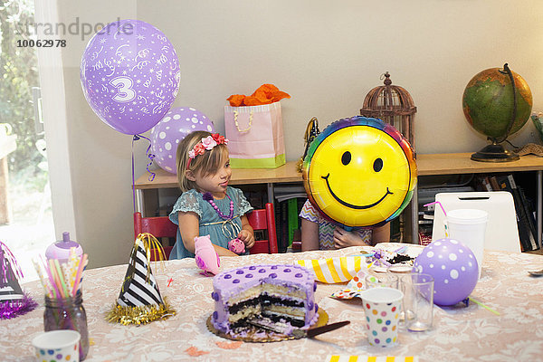 Zwei Mädchen sitzen am Geburtstagstisch und spielen mit einem Smiley-Ballon.