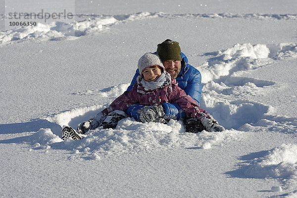 Vater und Tochter sitzen im tiefen Schnee  Bad Heilbrunn  Oberbayern  Bayern  Deutschland  Europa