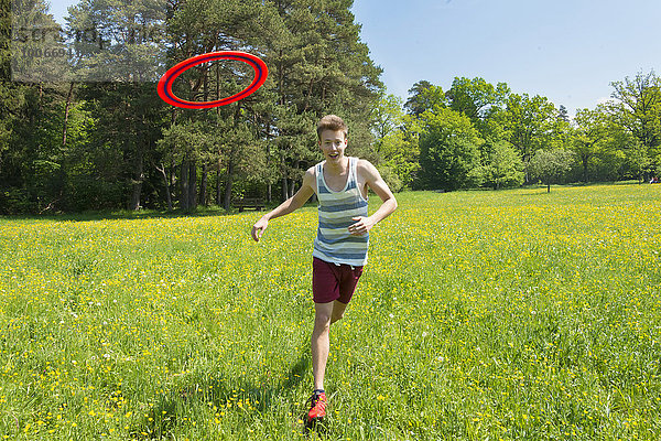 Junger Mann läuft Frisbee hinterher  gelbe Blumenwiese  Perlacher Forst  München  Bayern  Deutschland  Europa