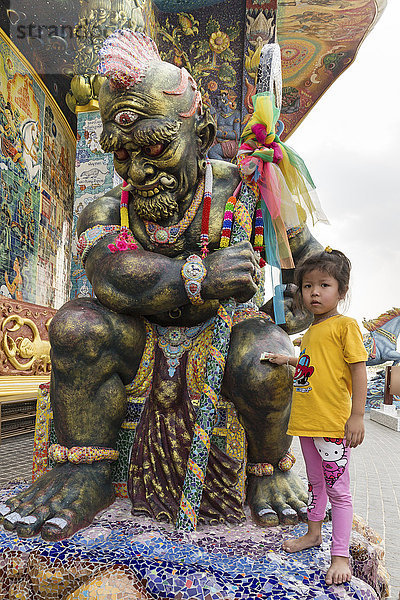 Mädchen reibt Geldschein an einer Yaksa-Statue  Yak  Elefanten-Tempel Thep Wittayakhom Vihara  Wittayakom  Wat Baan Rai  Korat  Nakhon Ratchasima Provinz  Isaan  Isan  Thailand  Asien