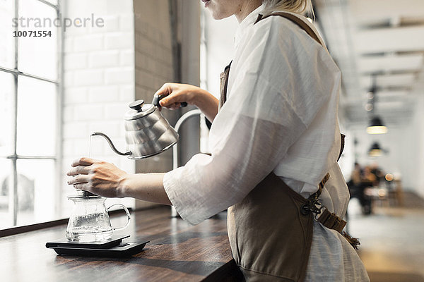 Seitenansicht Mittelteil des weiblichen Barista  der kochendes Wasser in den Kaffeefilter am Kaffeetresen gießt
