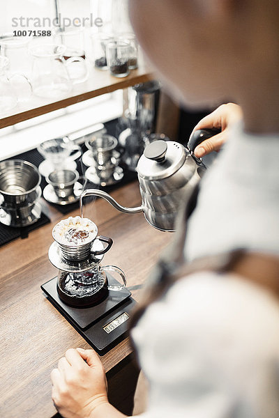 Hochwinkliges Bild von Barista  der kochendes Wasser in den Kaffeefilter am Tresen gießt.