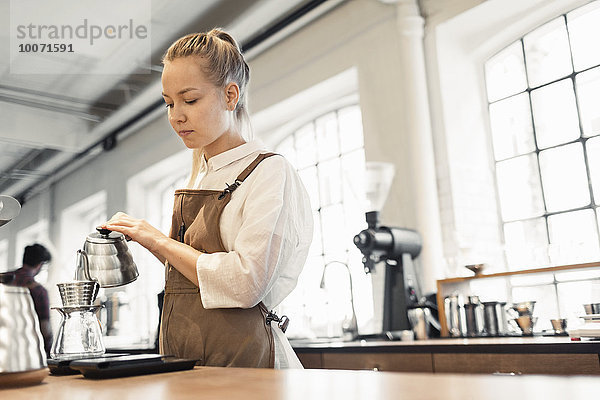 Weibliche Barista gießt kochendes Wasser in den Kaffeefilter im Cafe