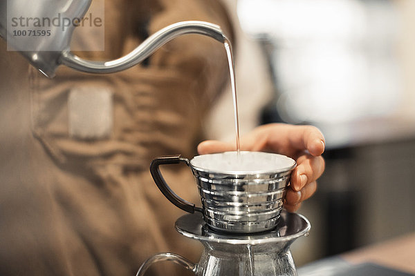 Abgeschnittenes Bild eines Barista  der Wasser in eine Kaffeetasse im Cafe gießt.