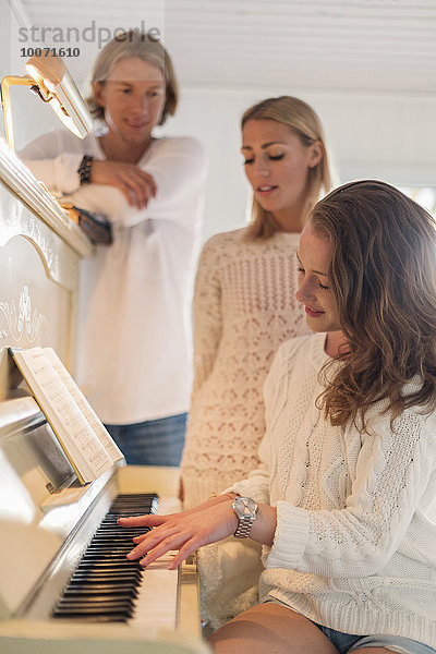 Freunde  die eine Frau beim Klavierspielen zu Hause beobachten.