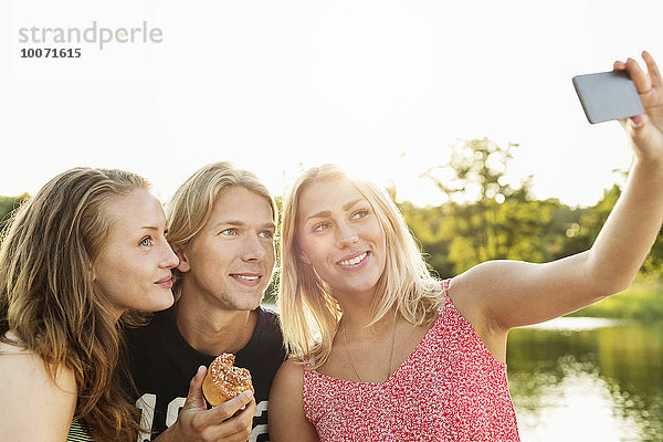 Fröhliche Freunde beim Frühstück am See bei klarem Himmel