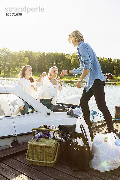 Freunde beim Entladen des Gepäcks vom Boot am Pier gegen den klaren Himmel