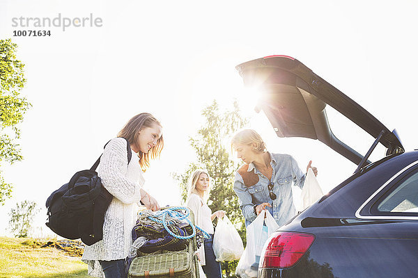 Männliche und weibliche Freunde  die das Auto auf dem Feld gegen den klaren Himmel entladen.