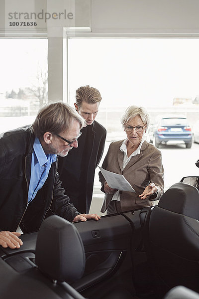 Senior Verkäuferin erklärt der Familie im Geschäft die Eigenschaften des Autos