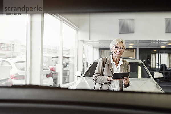 Senior Geschäftsfrau mit digitalem Tablett beim Blick auf das Auto im Geschäft