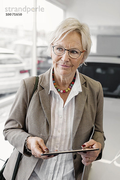 Senior Geschäftsfrau mit digitalem Tablett stehend im Autohaus