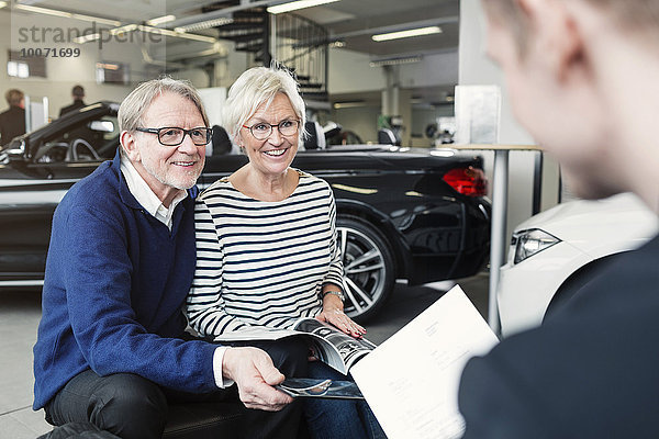 Glückliches Senior-Paar beim Anblick des Verkäufers im Autohaus
