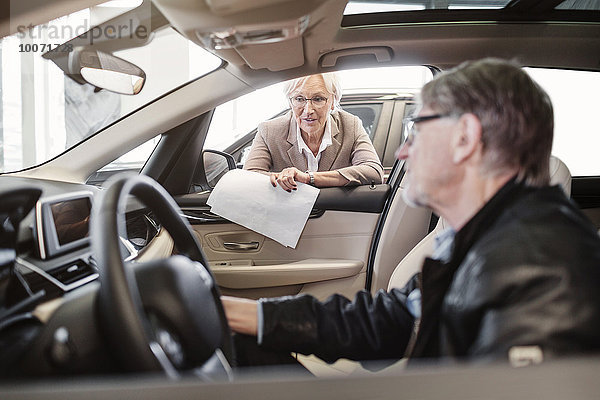 Senior Verkäuferin erklärt dem Mann  der im Auto im Geschäft sitzt.