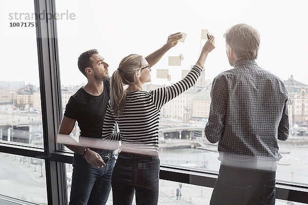 Geschäftsleute diskutieren über Haftnotizen am Glasfenster