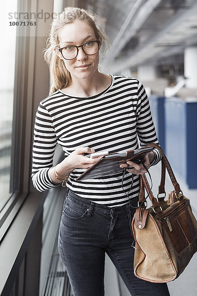 Porträt einer selbstbewussten Geschäftsfrau mit Handy und digitalem Tablett im Büro