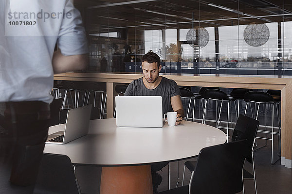 Geschäftsmann mit Laptop am Tisch im Bürocafé