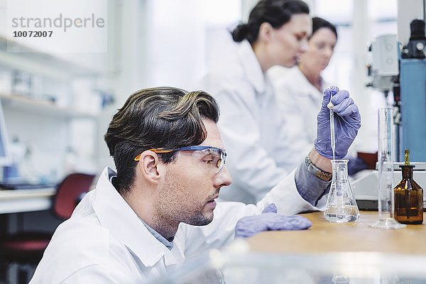Männlicher Wissenschaftler untersucht Probe im Labor mit weiblichen Kollegen im Hintergrund