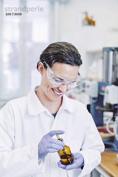 Glückliche Wissenschaftlerin mit Pipette bei der Untersuchung von Chemikalien im Labor