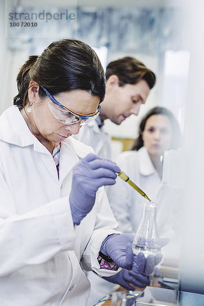 Wissenschaftlerin untersucht Probe im Labor mit Kollegen im Hintergrund