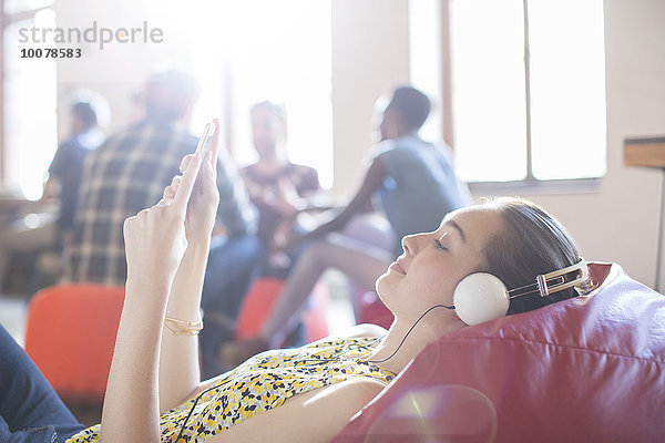 Lässige Geschäftsfrau beim Entspannen mit Kopfhörer und digitalem Tablett auf Bohnensäckchenstuhl
