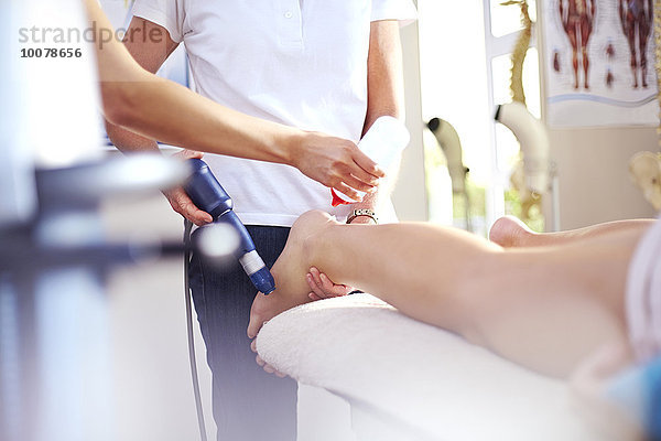 Masseurin beim Auftragen des Gels auf das Bein der Frau zur Vorbereitung der Ultraschallsonde
