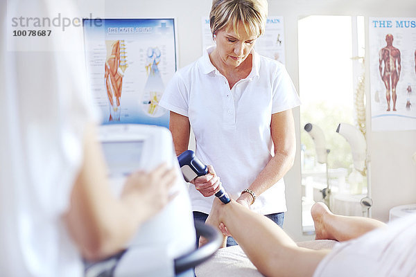 Physiotherapeutin mit Ultraschallsonde am Bein der Frau