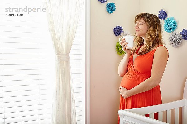 Schwangere Frau trinkt Kaffee und träumt im Kinderzimmer