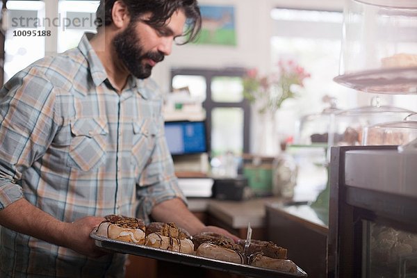 Bäckereibesitzer stellt Tablett mit veganen  allergikerfreundlichen Donuts in die Vitrine