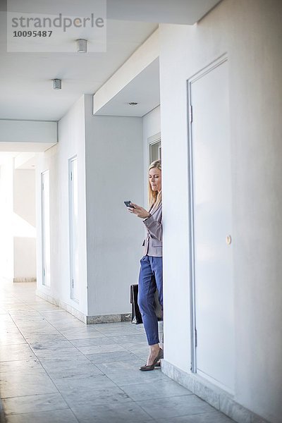 Mittlere erwachsene Geschäftsfrau liest Smartphone-Text im Hotelkorridor