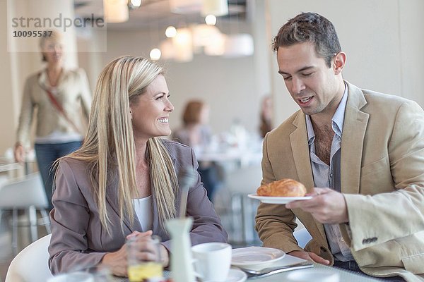 Geschäftsmann übergibt Croissant an Kollegen beim Frühstück im Hotelrestaurant