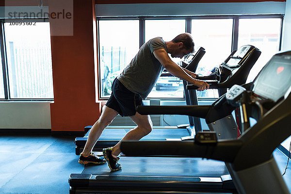 Erschöpfter erwachsener Mann  der sich auf dem Laufband nach vorne lehnt.