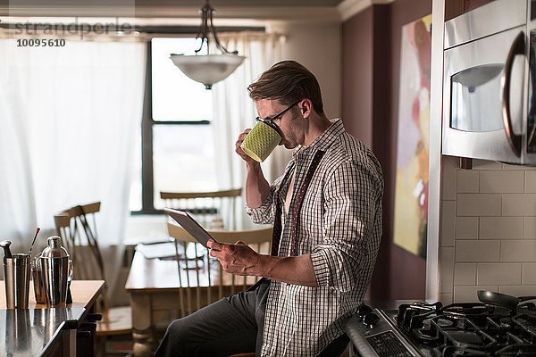 Mittlerer Erwachsener Mann in der Küche  der Kaffee trinkt  während er digitales Tablett liest.