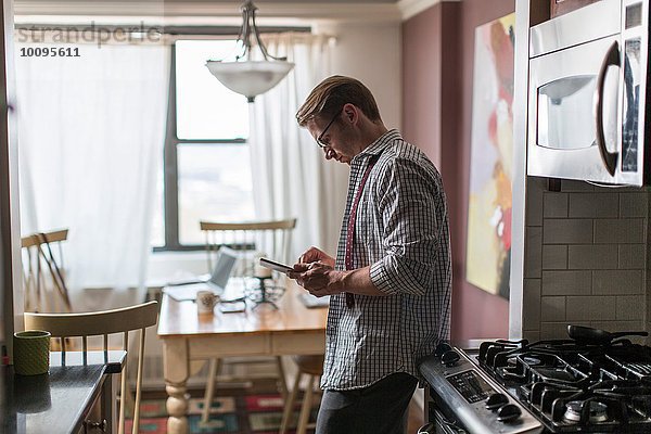 Mittlerer Erwachsener Mann in der Küche mit Touchscreen auf digitalem Tablett