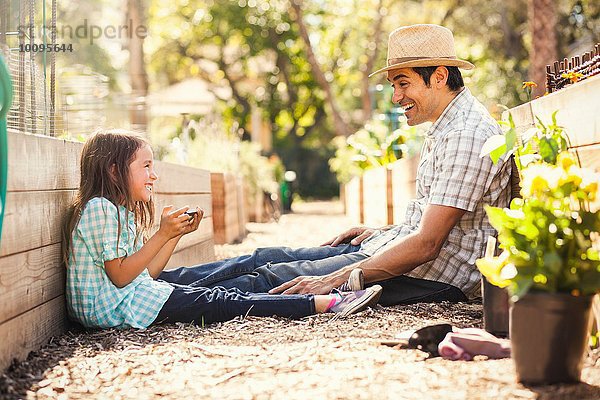 Mädchen mit Väter-Smartphone im Gemeinschaftsgarten