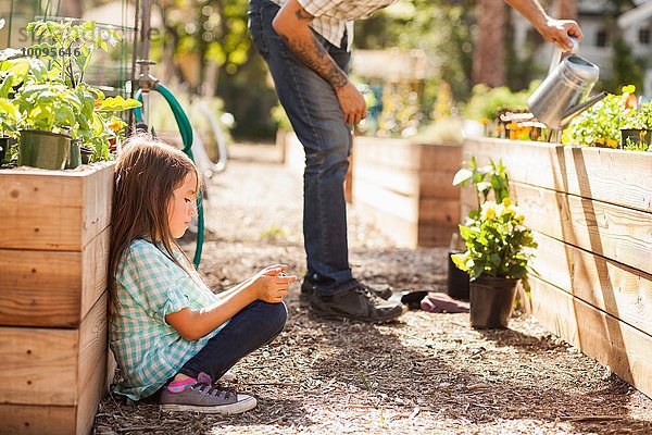 Mädchen hocken im Gemeinschaftsgarten mit dem Smartphone